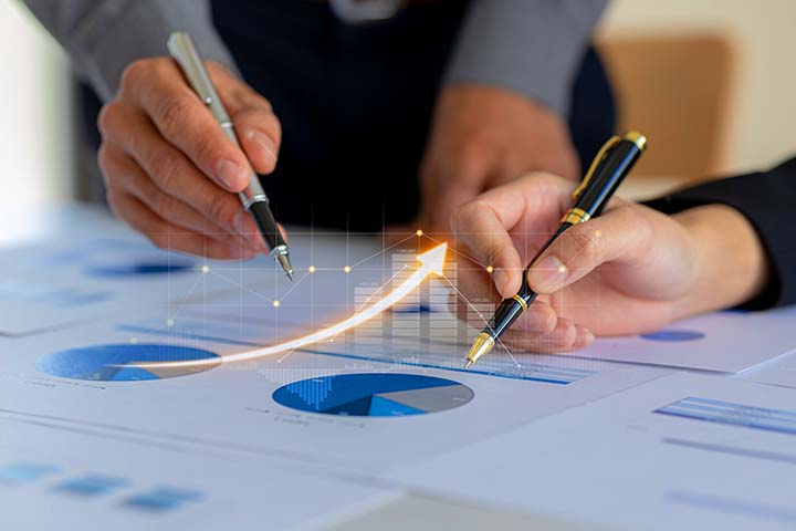 Two businessmen are meeting together, they point to financial documents to discuss plans and solutions, chart graphics showing financial status and performance. Business administration concept.
